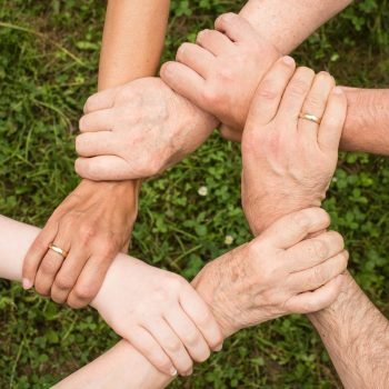 Close-up of diverse hands forming a connection, symbolizing teamwork and unity outdoors.